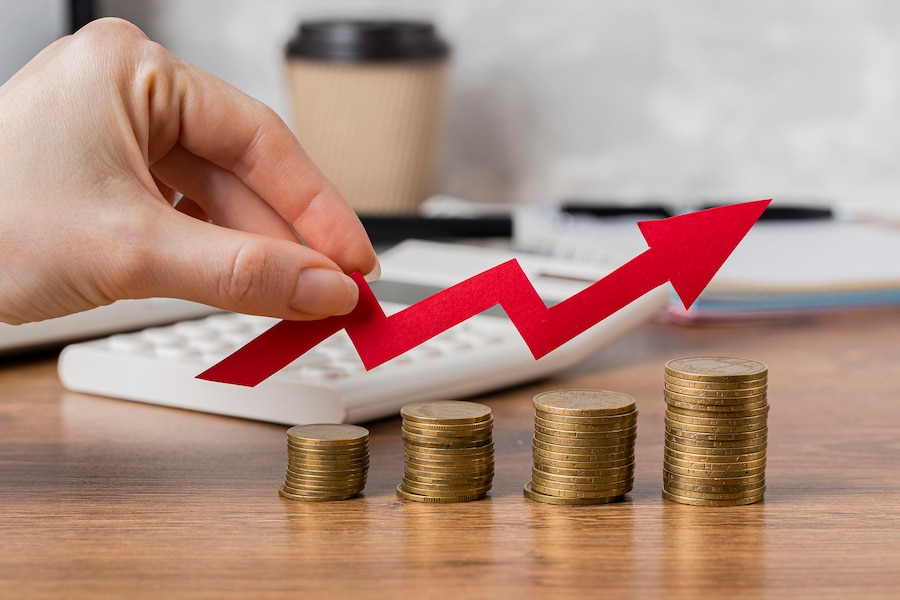 Hand drawing a red upward arrow above rising stacks of coins, suggesting a growing balance