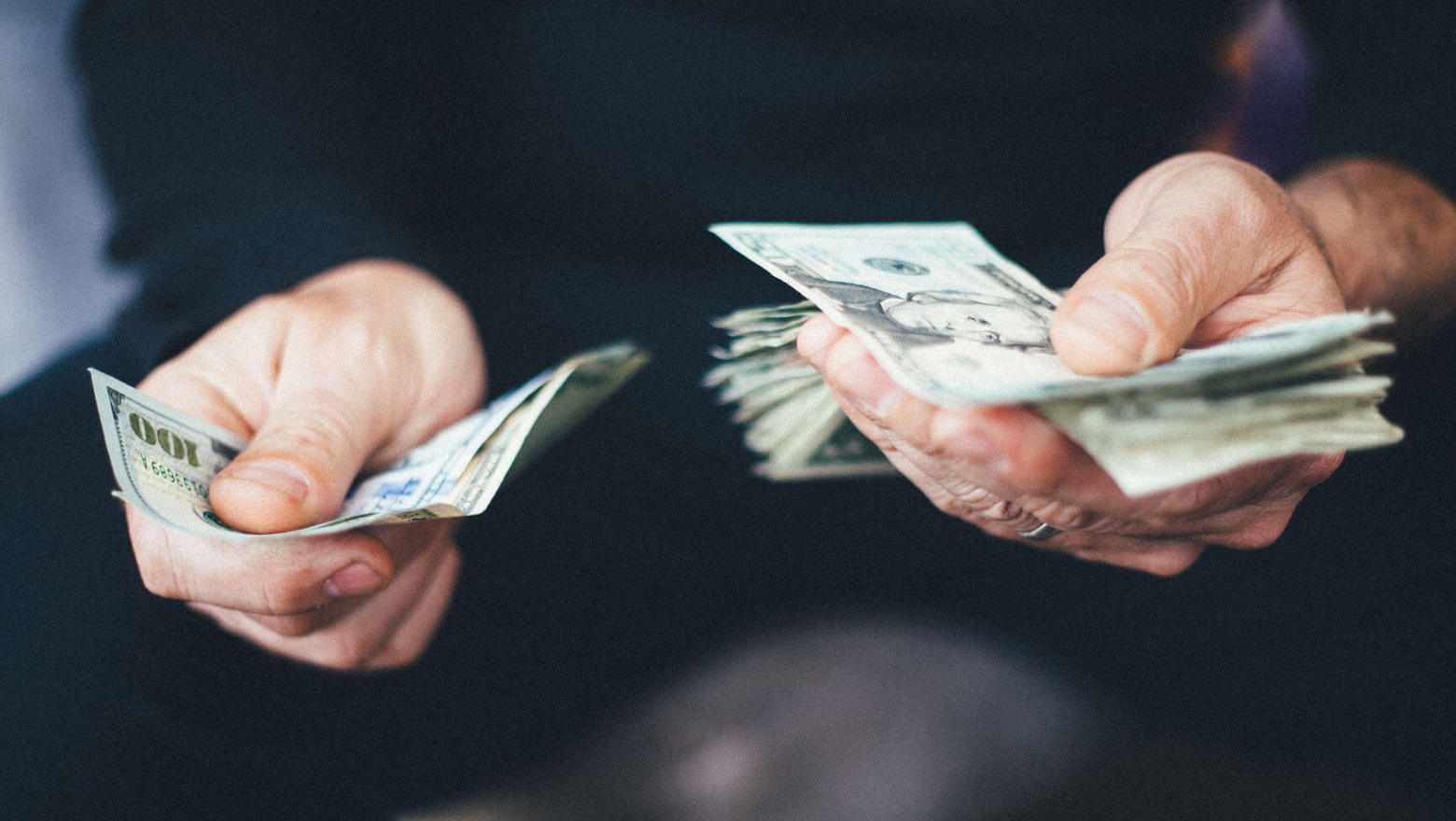 Two hands holding and counting US dollar banknotes against a dark background
