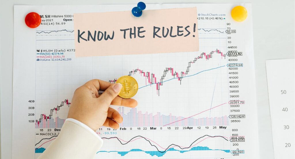 “Know the Rules!” note pinned on a stock chart while a hand holds a gold Bitcoin coin