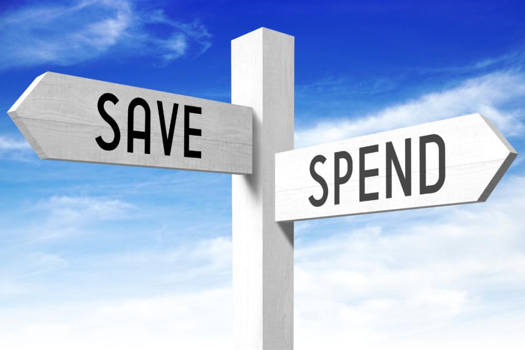 Road signpost pointing in two directions, “Save” and “Spend”, against a blue sky